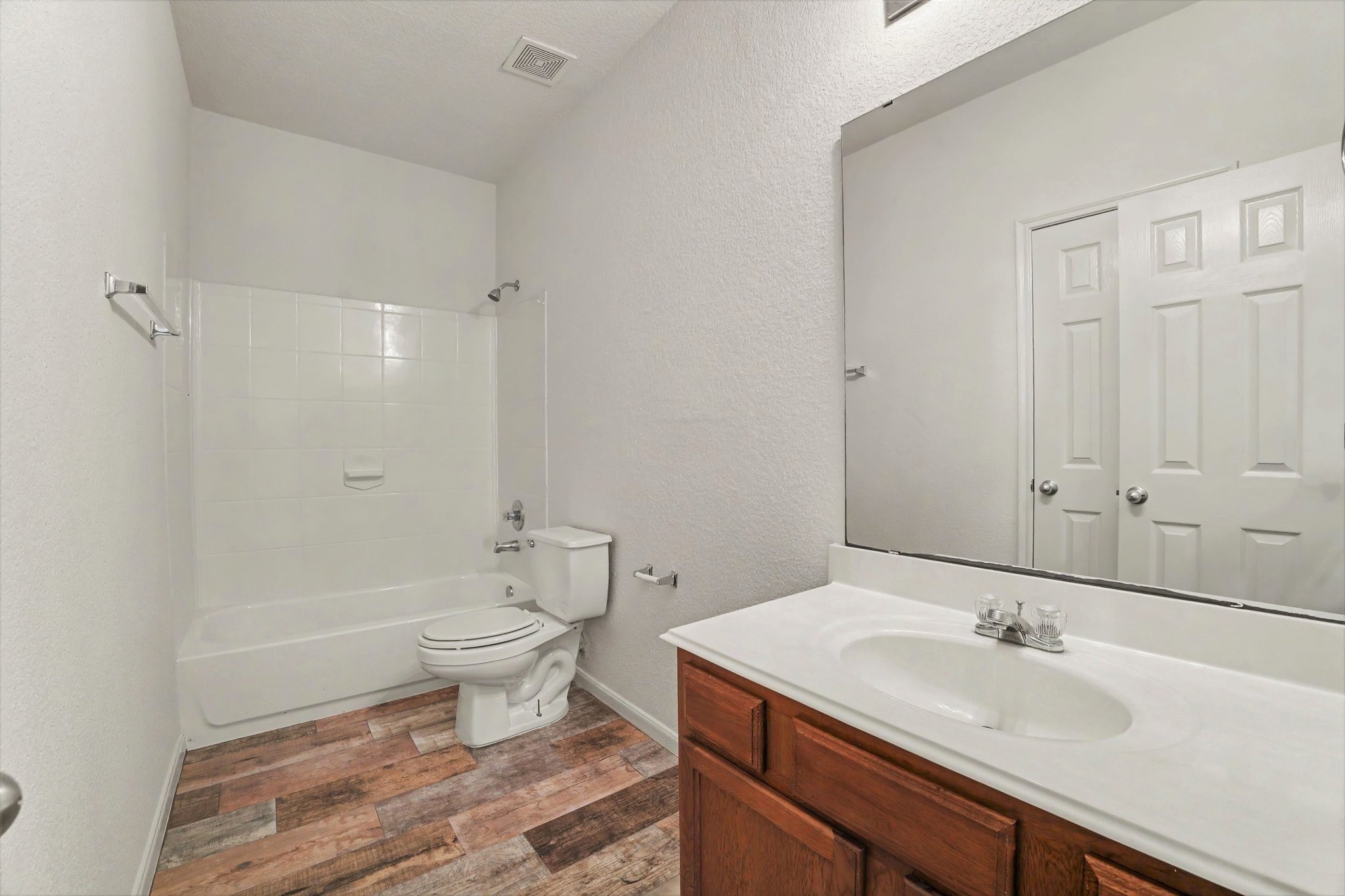 21427 Blooming Rock Lane Spring, TX 77379 - Photo 14 of 32 This bathroom features a clean, modern design with a white bathtub and shower, a large mirror above a single-sink vanity, and wood-look flooring.