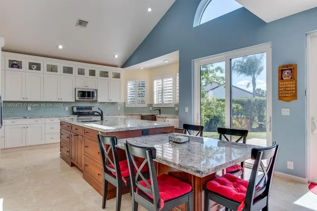 a kitchen with stainless steel appliances granite countertop a dining table chairs and window
