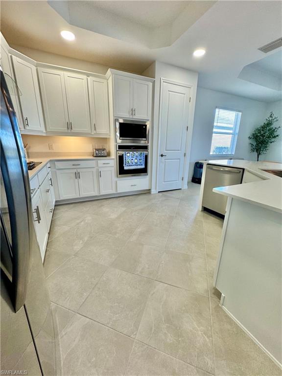 5376 Fancourt Links Way Ave Maria, FL 34142 - Photo 6 of 39 Kitchen with recessed lighting, a raised ceiling, white cabinets, stainless steel appliances, and light stone countertops
