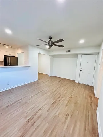 a view of an empty room with wooden floor and a ceiling fan