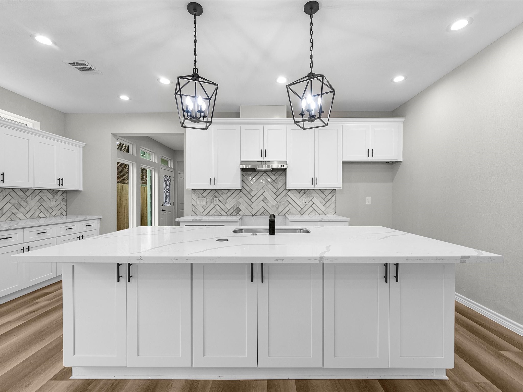 1319 West Bell Street Houston, TX 77019 - Photo 15 of 50 Modern kitchen with white cabinetry and a spacious island featuring a marble countertop. The room includes geometric pendant lighting and a stylish herringbone backsplash. Vinyl flooring adds warmth to the space.