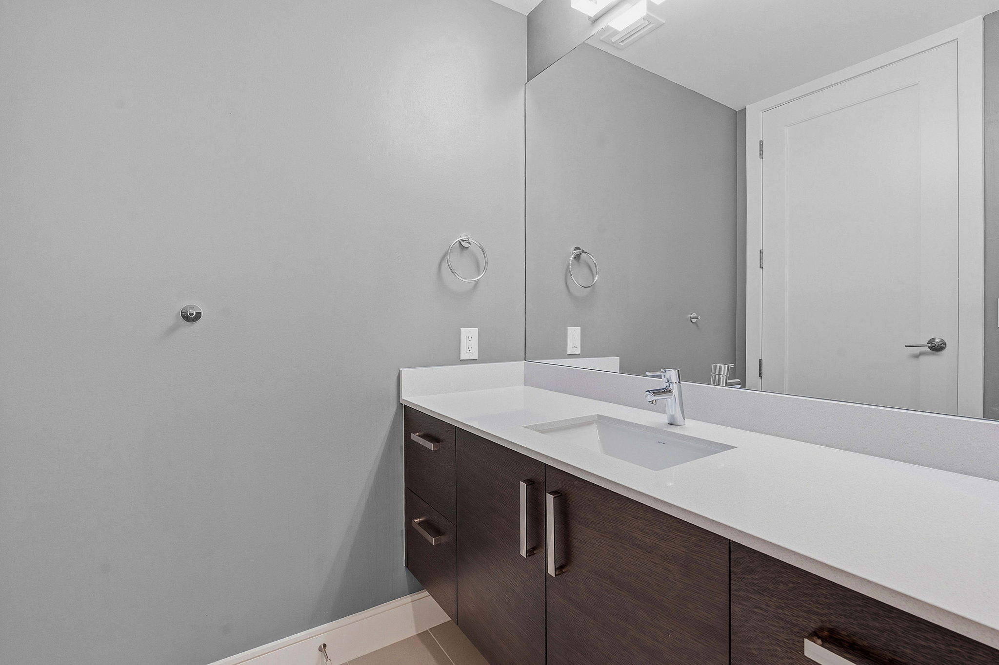222 West Avenue, Unit 2207 Austin, TX 78701 - Photo 10 of 30 Modern vanity featuring a white countertop with integrated sink, chrome faucet, dark wood-finish cabinetry, and a full-width mirror