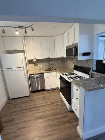 a kitchen with granite countertop a refrigerator a stove top oven a sink and white cabinets