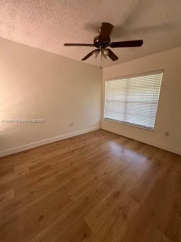 an empty room with wooden floor fan and windows
