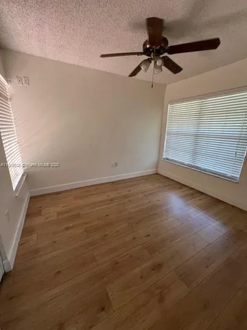 an empty room with wooden floor fan and windows