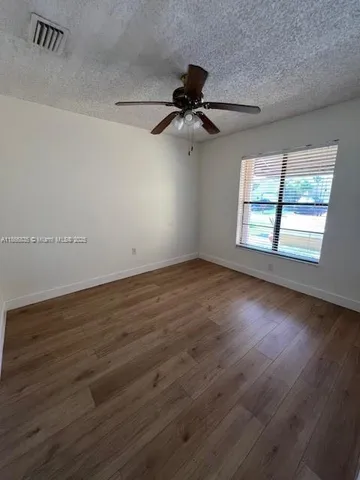 an empty room with wooden floor fan and windows