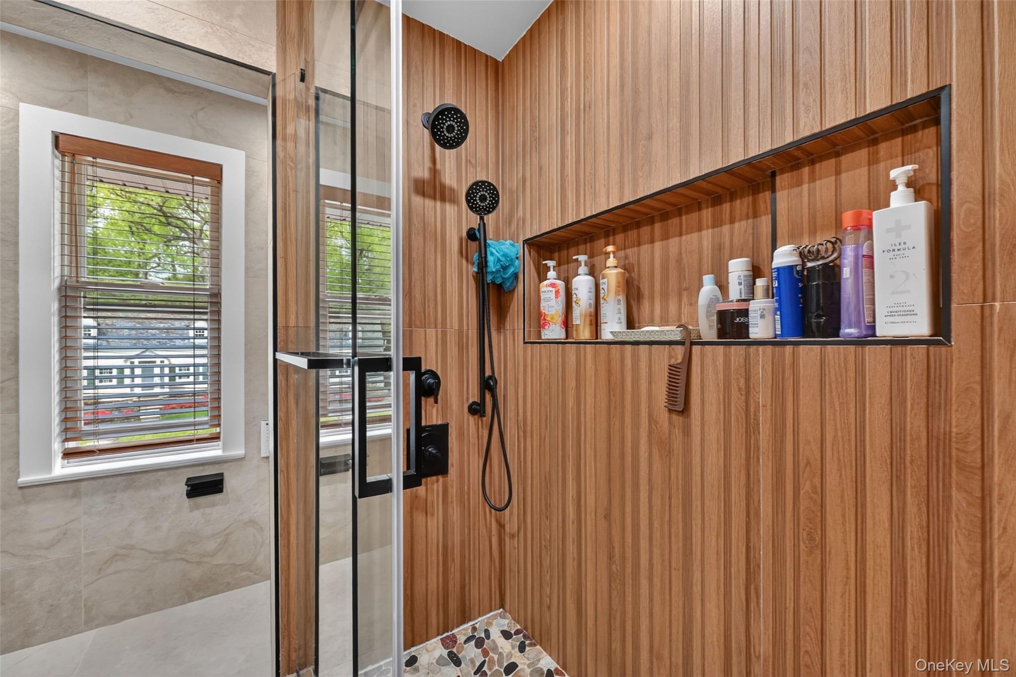 65 Wildway Bronxville, NY 10708 - Photo 31 of 42 Shower enclosure featuring glass doors, wood-finish wall panels, a built-in recessed shelf with a dark frame, and matte black shower fixtures