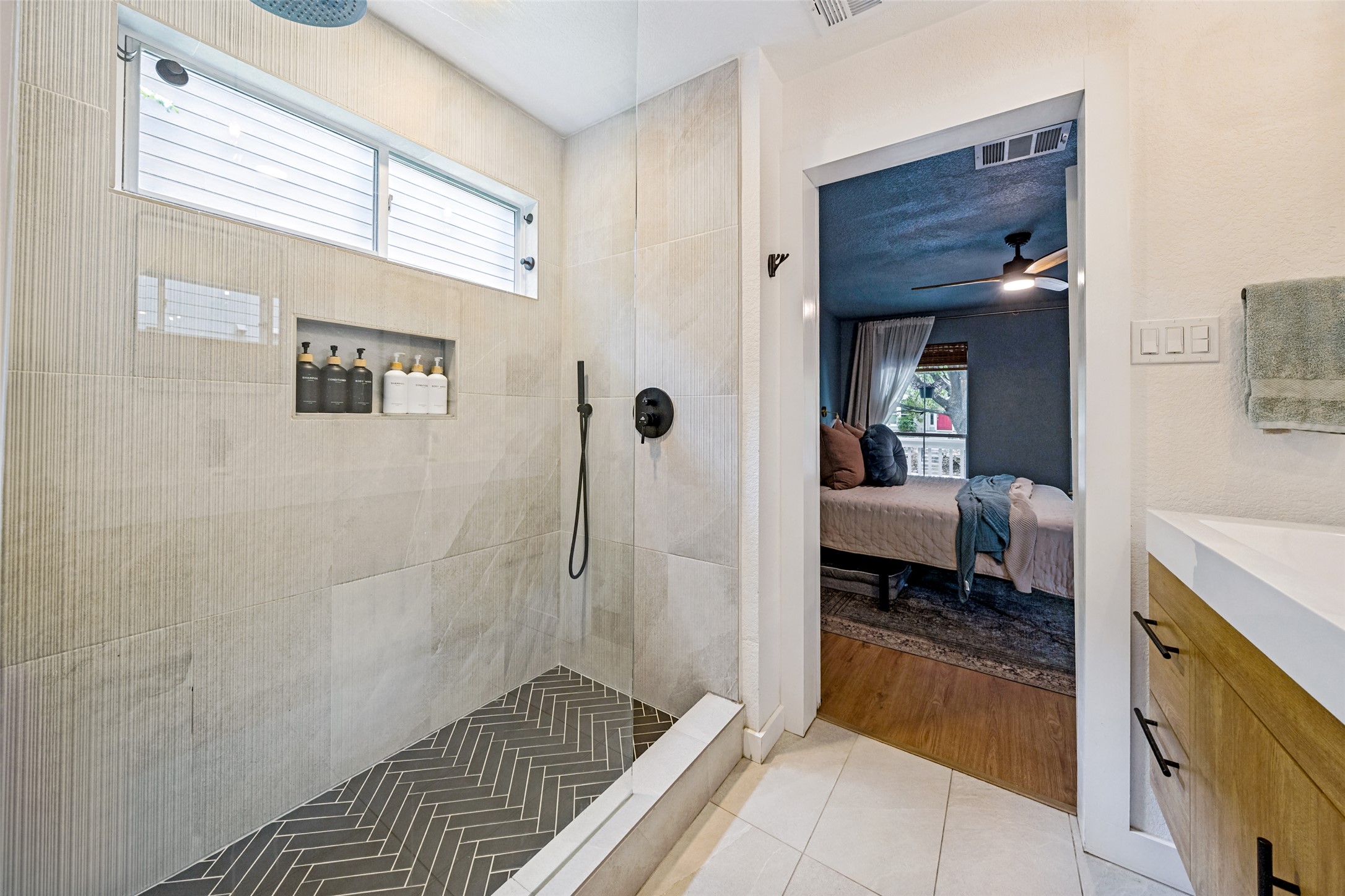 9205 Rowlands Sayle Road Austin, TX 78744 - Photo 18 of 25 A modern tiled shower with a niche for toiletries adjoins a bedroom with wood flooring.