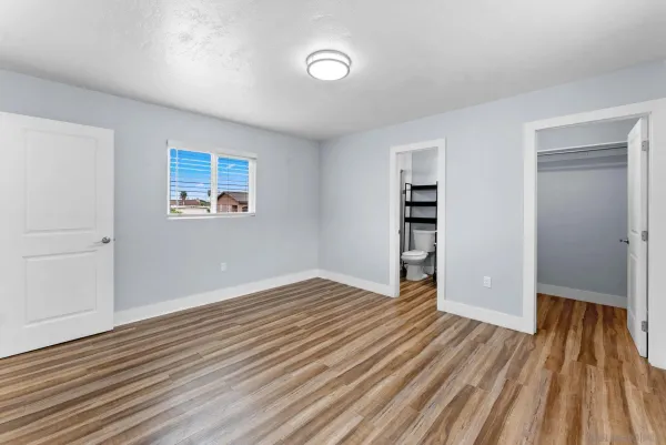 an empty room with wooden floor closet and windows