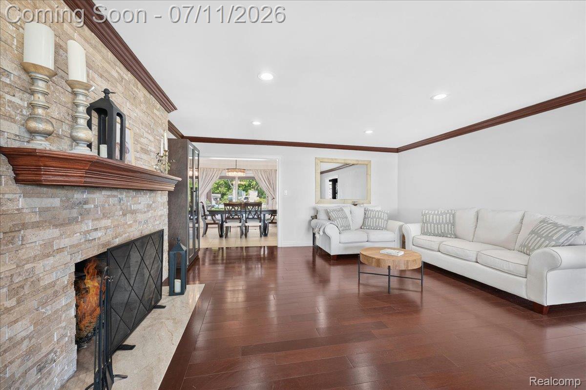 23750 East River Road Grosse Ile, MI 48138 - Photo 7 of 54 Spacious living area featuring a stacked stone fireplace with a substantial wood mantel, rich wood-finish flooring, recessed lighting, and crown molding