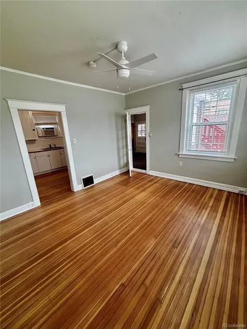 a view of an empty room with wooden floor kitchen view and a window