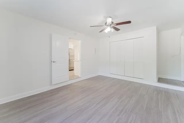 an empty room with wooden floor fan and windows