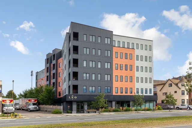 a front view of a building with lot of cars and trees