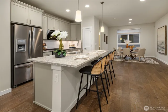 a kitchen with stainless steel appliances kitchen island granite countertop a refrigerator a stove a sink a dining table and chairs with wooden floor