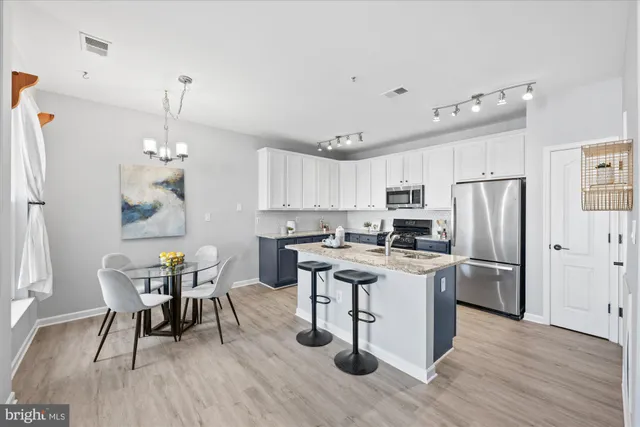 a kitchen with stainless steel appliances granite countertop a refrigerator a stove top oven a sink dishwasher a dining table and chairs with wooden floor