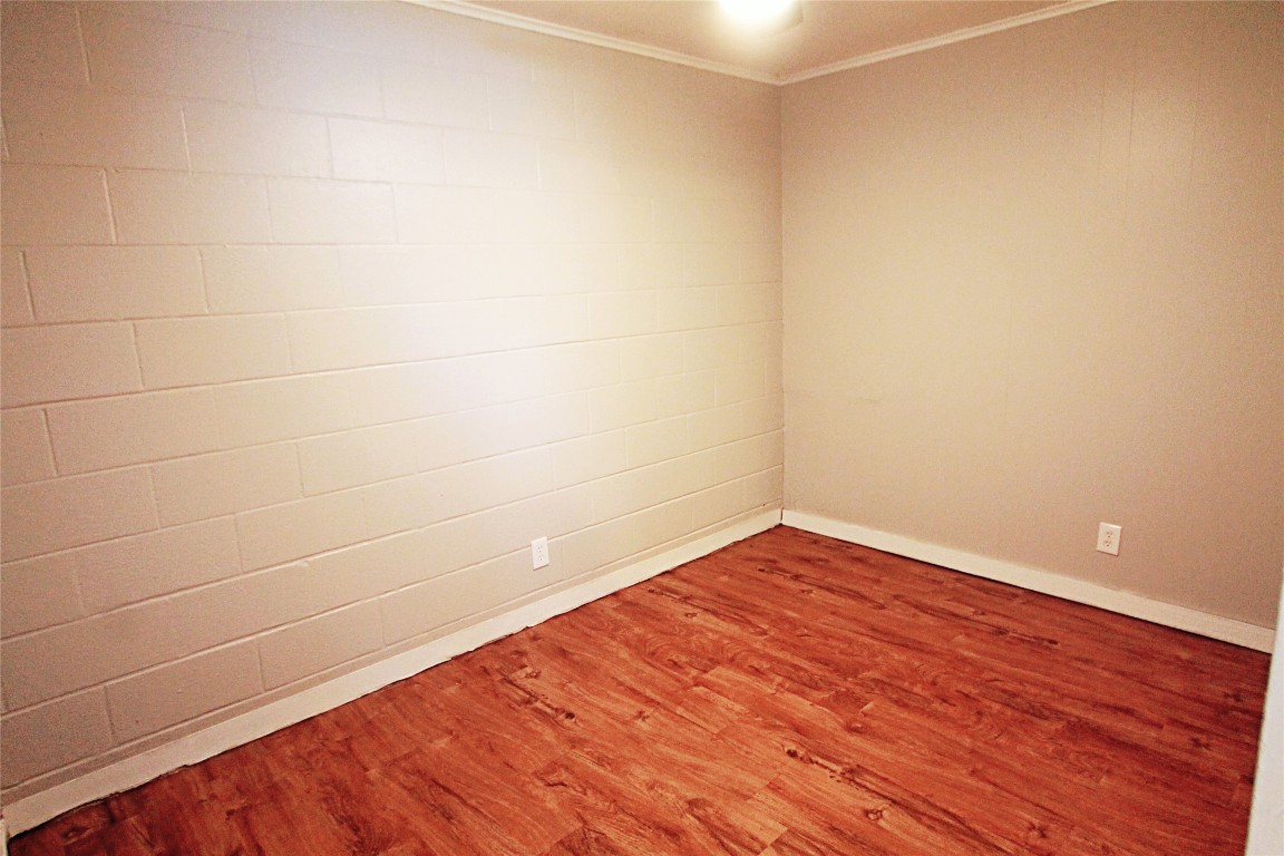 901 Springdale Road, Unit 102 Austin, TX 78702 - Photo 10 of 17 Empty room featuring crown molding, wood finished floors, and concrete block wall