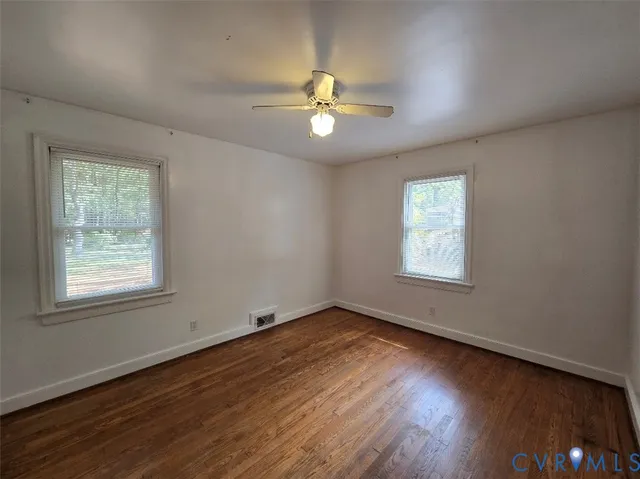an empty room with wooden floor ceiling fan and windows