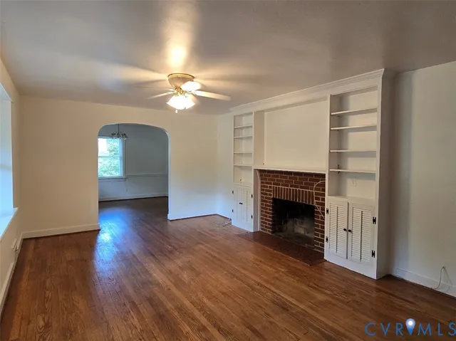 a view of an empty room with wooden floor fireplace and a window