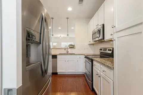 a kitchen with stainless steel appliances granite countertop a refrigerator a sink a stove and white cabinets