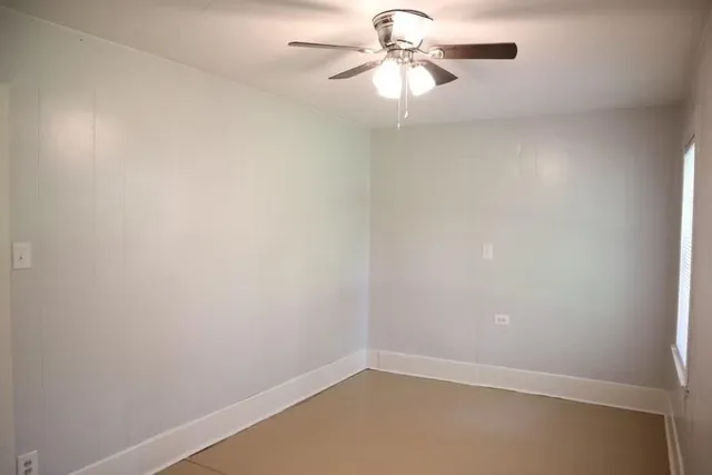 an empty room with a chandelier fan and windows