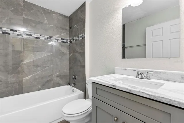 a bathroom with a granite countertop bathtub shower sink vanity mirror and toilet