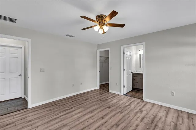 a view of an empty room with wooden floor and a ceiling fan