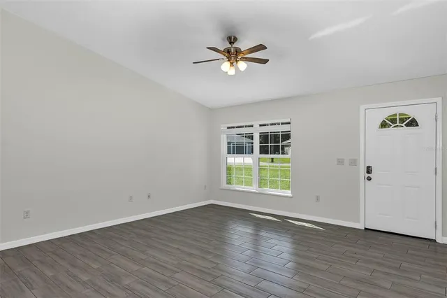 an empty room with wooden floor chandelier fan and windows