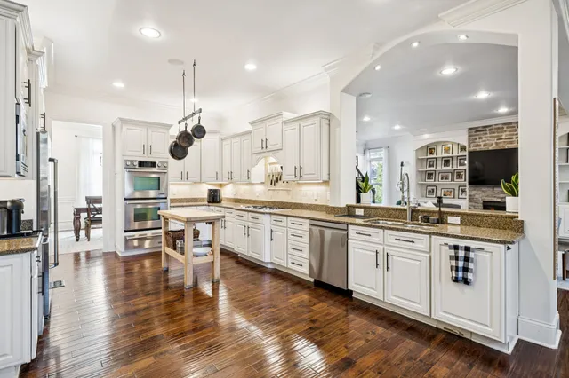 a kitchen with stainless steel appliances granite countertop a stove a sink a dining table and chairs with wooden floor