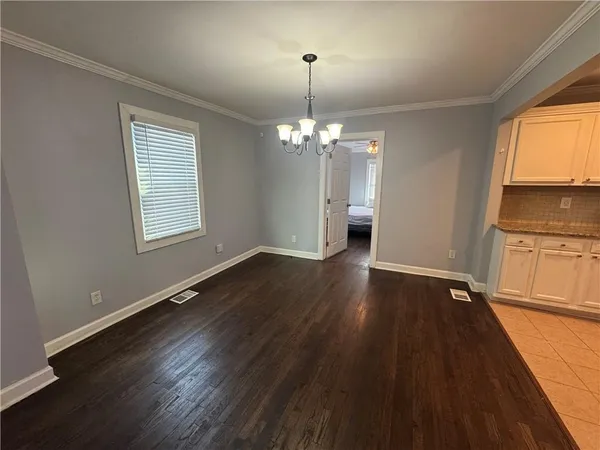 an empty room with wooden floor chandelier and windows