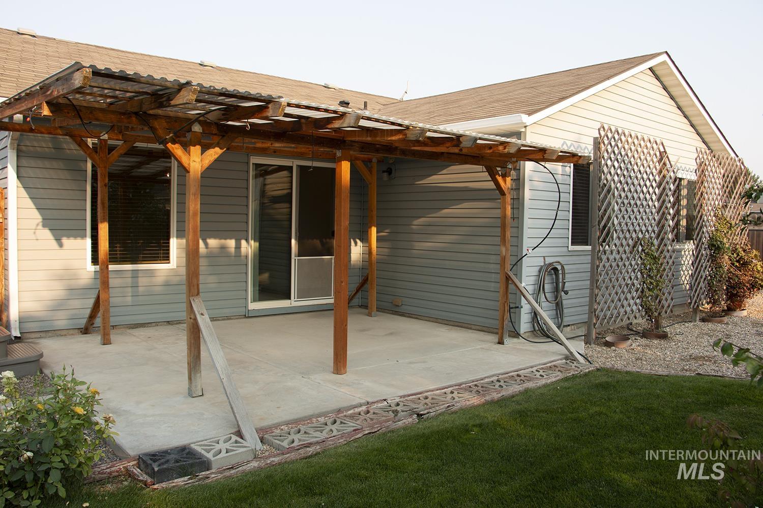 16559 Bayou Way Caldwell, ID 83607 - Photo 19 of 20 Concrete patio featuring a wood pergola with a corrugated roof, siding exterior, sliding glass door, and a gravel bed with trellises