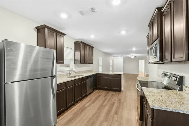 a large kitchen with stainless steel appliances granite countertop a refrigerator a sink dishwasher a stove and a refrigerator with wooden floor