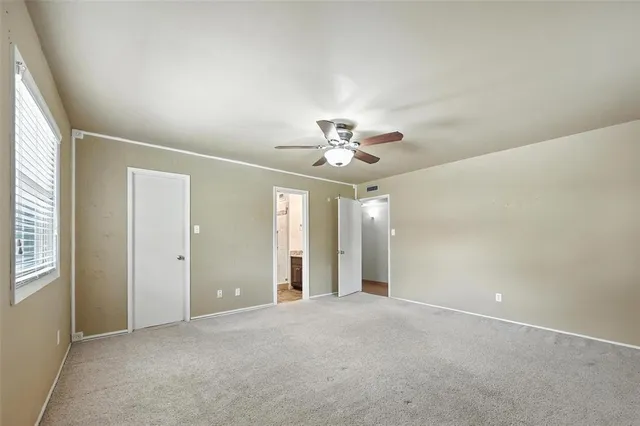 an empty room with chandelier fan and windows