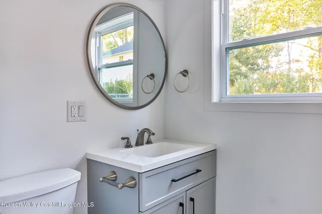 a bathroom with a sink a mirror a toilet and a window