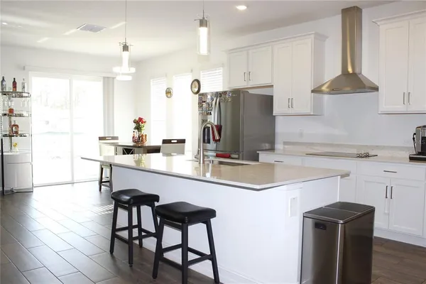 a kitchen with stainless steel appliances kitchen island granite countertop a sink a stove a refrigerator and white cabinets with wooden floor