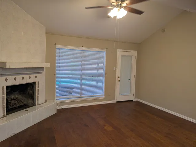 a view of an empty room with wooden floor fireplace and a window