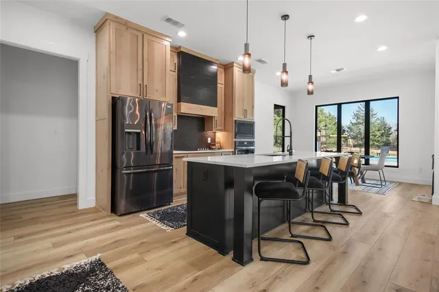 a kitchen with stainless steel appliances kitchen island granite countertop a refrigerator a oven a sink a dining table and chairs with wooden floor