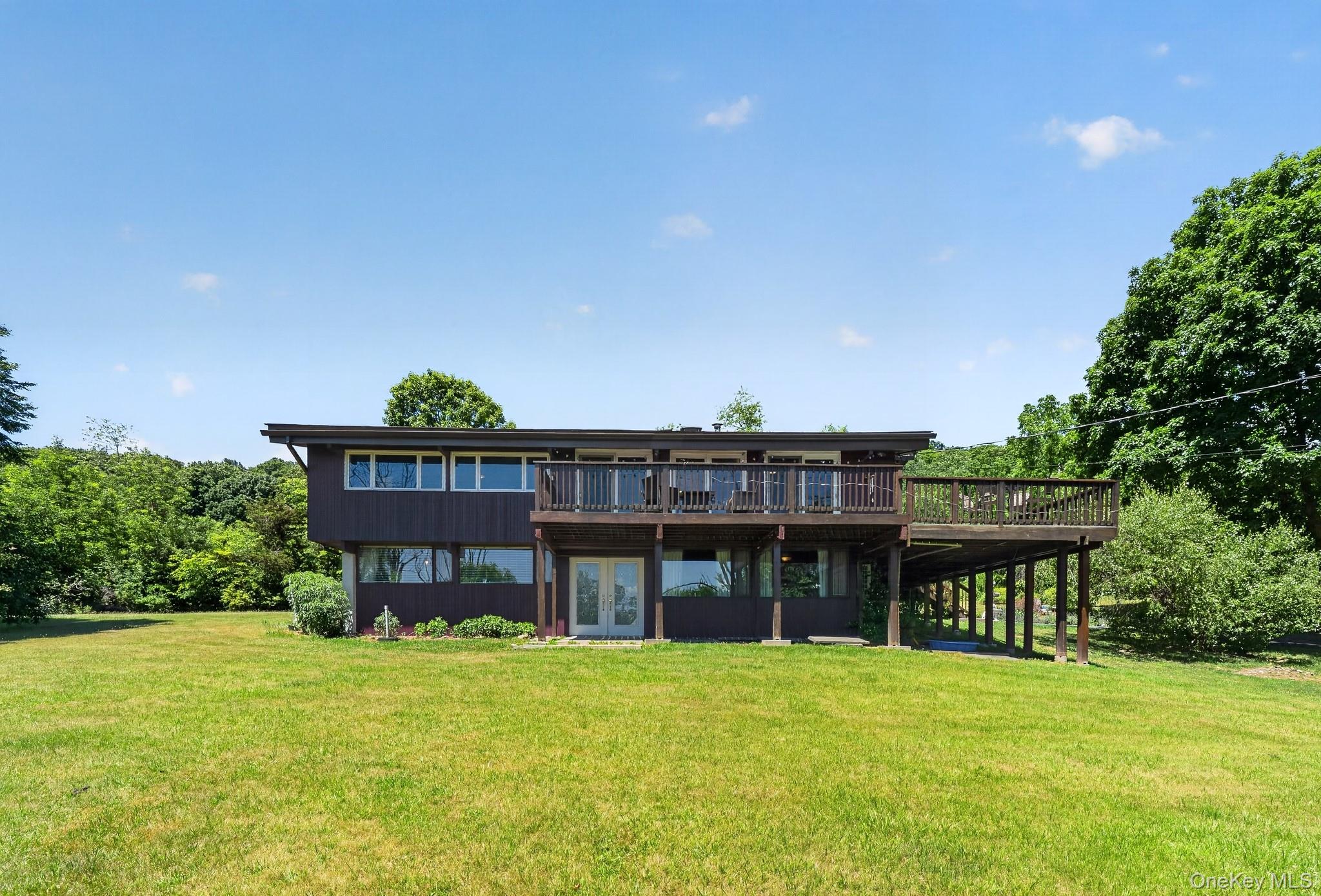 424 Laroe Road Chester, NY 10918 - Photo 19 of 43 Contemporary two-story residence featuring a dark brown exterior, expansive upper-level deck with wooden railing, and a lower-level patio with French doors