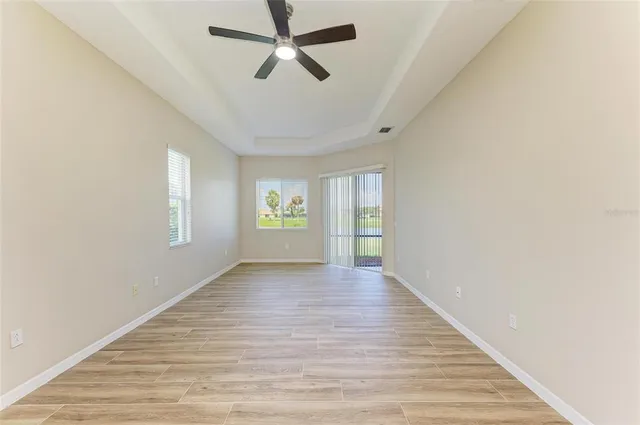 an empty room with a chandelier fan and wooden floor