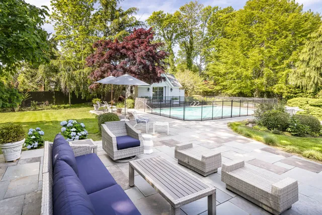 a view of a patio with couches table and chairs under an umbrella with large trees