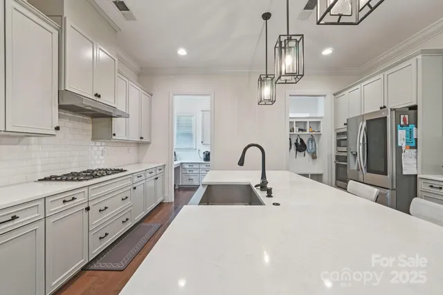 a kitchen with stainless steel appliances kitchen island a refrigerator a sink dishwasher a stove and white cabinets with wooden floor