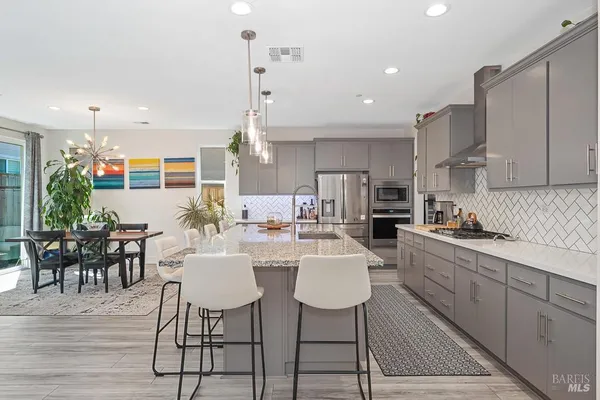 a kitchen with stainless steel appliances kitchen island granite countertop a dining table chairs and white cabinets