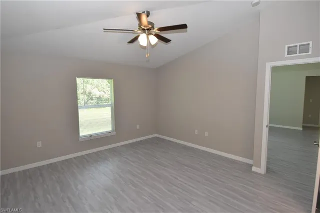 an empty room with wooden floor fan and windows