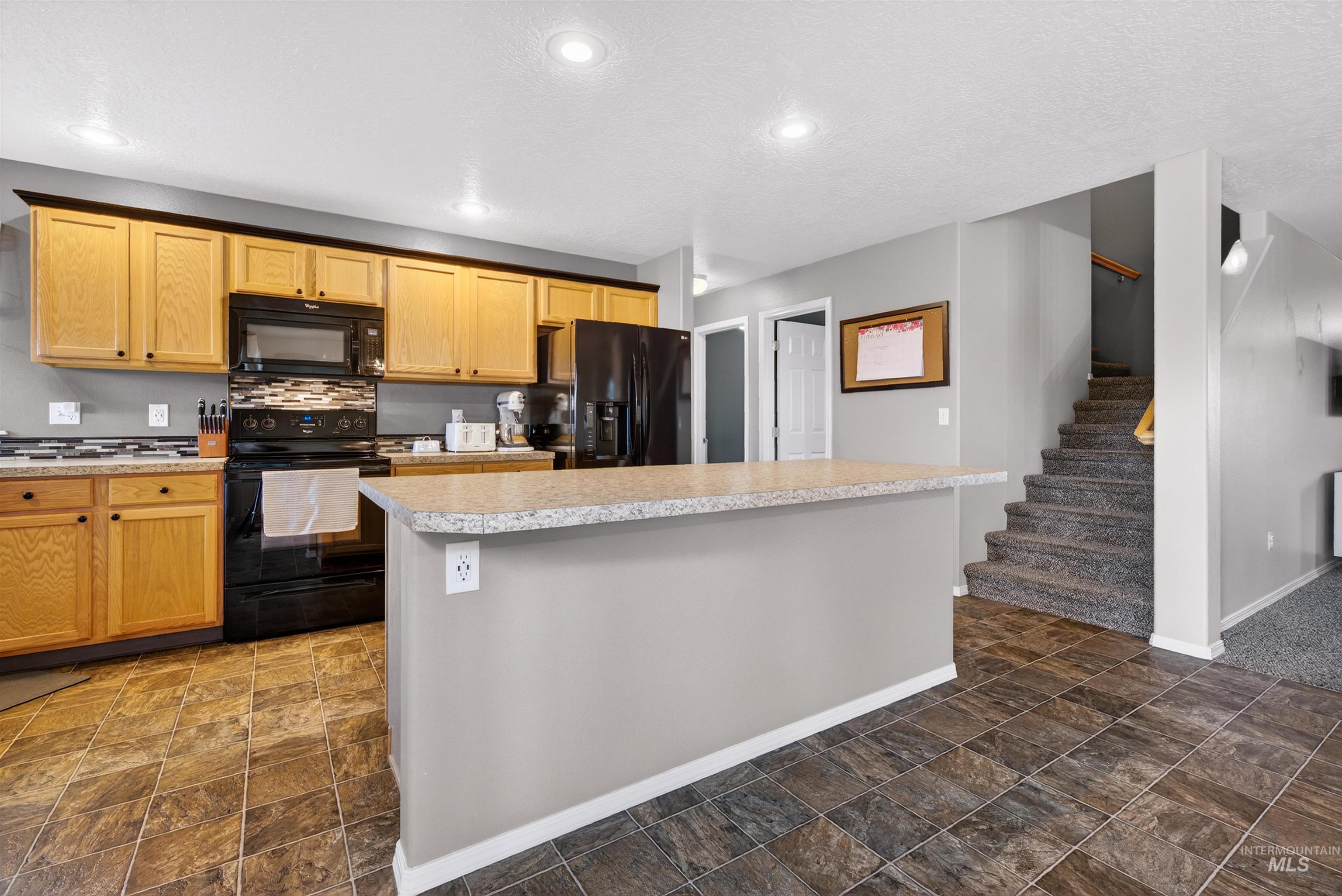 5414 Barkley Way Caldwell, ID 83607 - Photo 11 of 50 Kitchen with black appliances, light countertops, a kitchen island, and dark stone finish floors