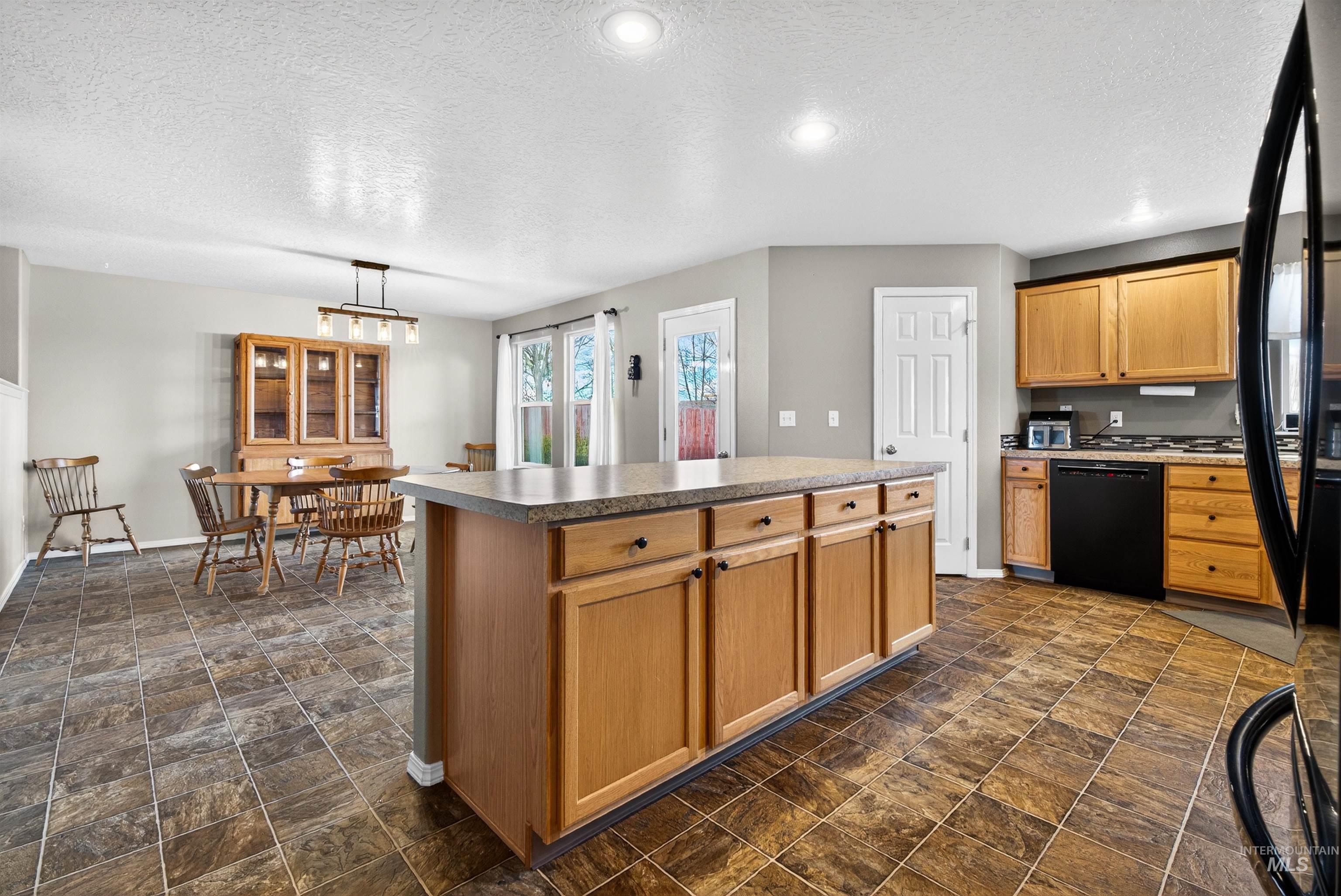 5414 Barkley Way Caldwell, ID 83607 - Photo 12 of 50 Kitchen featuring stone finish flooring, black appliances, a textured ceiling, pendant lighting, and a kitchen island