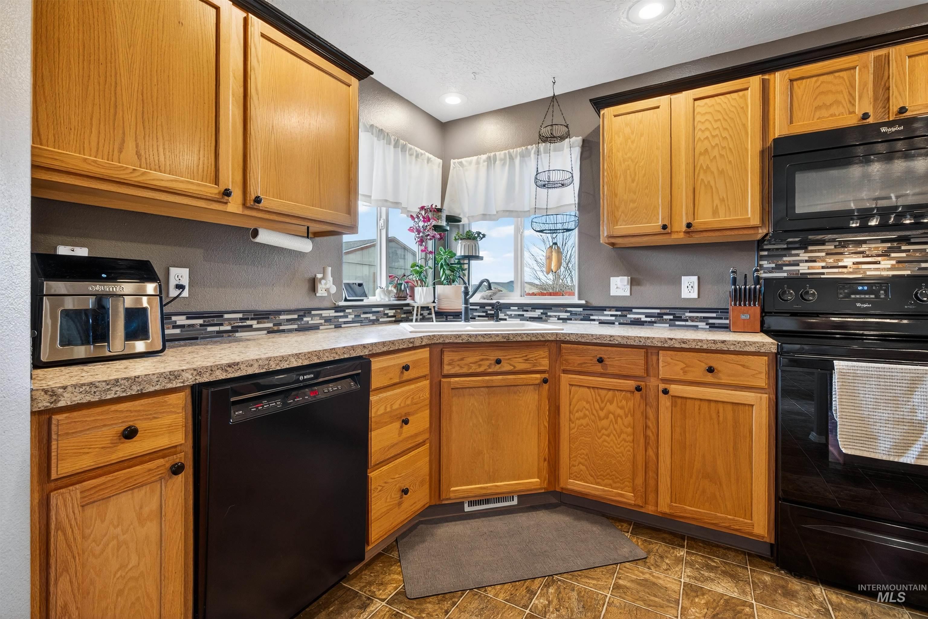 5414 Barkley Way Caldwell, ID 83607 - Photo 9 of 50 Kitchen with black appliances, light countertops, wood finish cabinetry, a textured ceiling, and tasteful backsplash