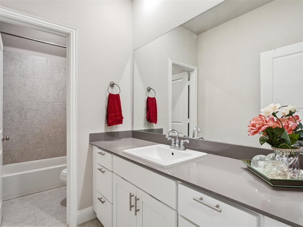 1128 Red Hawk Lane Forney, TX 75126 - Photo 29 of 37 Bathroom featuring a vanity with an integrated sink, polished chrome faucet, stone-finish countertop, white cabinetry with brushed nickel hardware, and an adjacent full-size bathtub with tiled surround