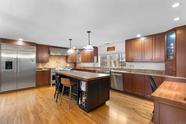 a kitchen with stainless steel appliances granite countertop a stove a sink dishwasher a refrigerator and a dining table with wooden floor