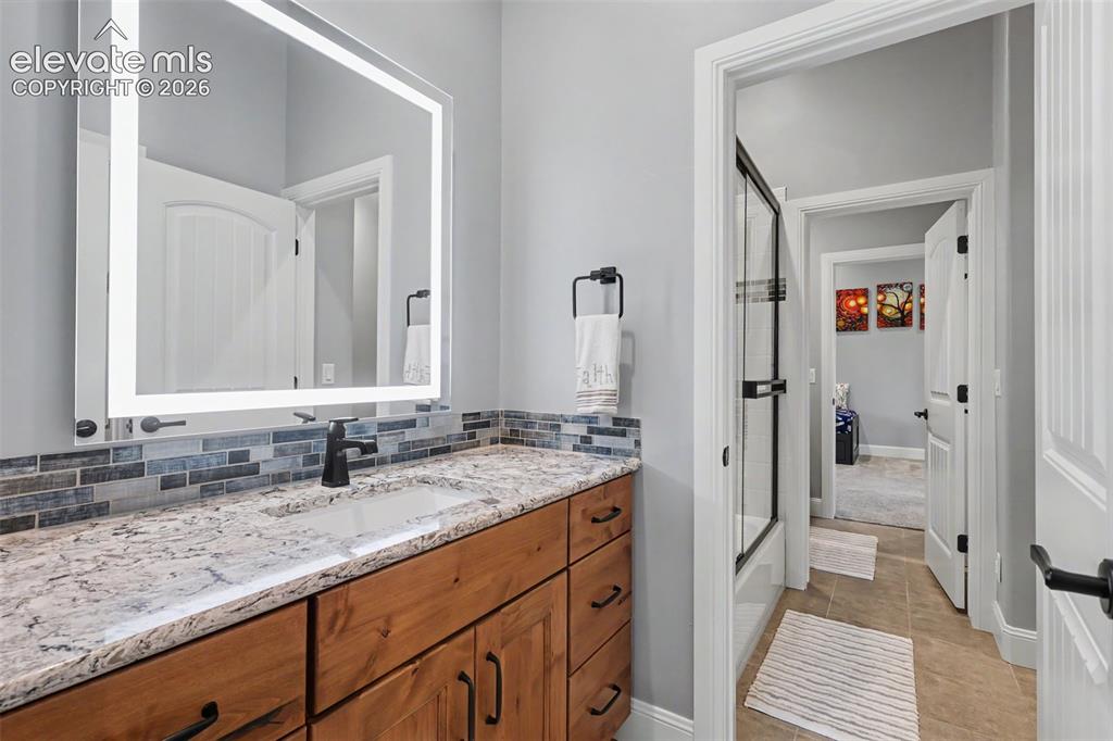 21 Leaming Road Colorado Springs, CO 80906 - Photo 43 of 48 Bathroom vanity featuring a granite countertop, integrated sink, matte black faucet, and a backlit mirror