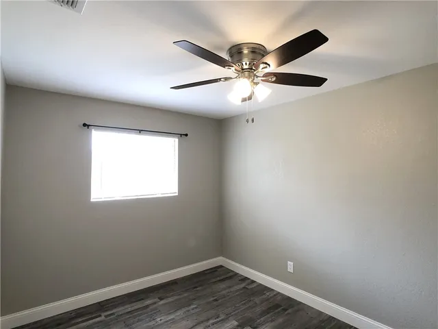 an empty room with wooden floor fan and windows