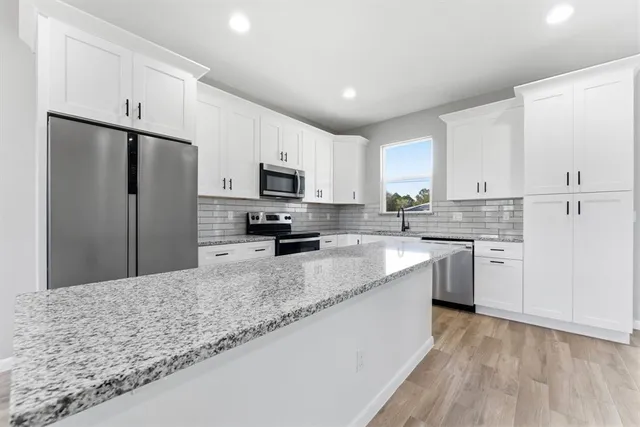 a kitchen with granite countertop a refrigerator a sink a stove a microwave and island